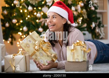 Happy biracial woman in santa hat lying under Christmas tree Stock Photo