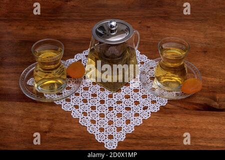 Linden herbal tea served with small glass tea set for two, with dry apricot on the wooden table. Stock Photo