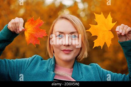 Smiling playful woman holding maple leaves in her hands from both sides of her face. Enjoy indian summer. Stock Photo