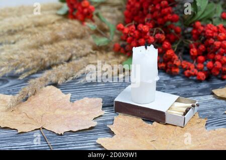 Orange pumpkin in a medical mask. Lies on black pine boards. Nearby is a bouquet of dried grass and mountain ash. There is a candle stub. Stock Photo