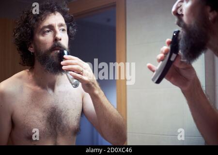 Middle-aged hispanic man cutting his beard Stock Photo