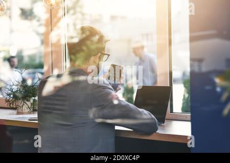 Important call. Rear view of a young businessman using his smartphone while working online in cafe Stock Photo