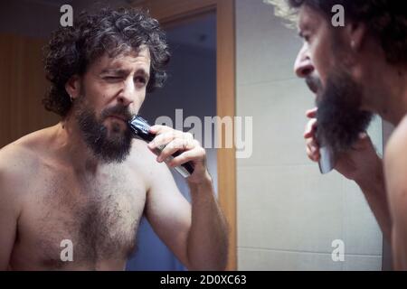 Middle-aged hispanic man cutting his beard Stock Photo