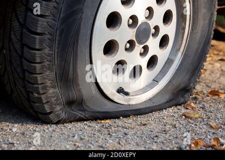 A car with a flat tire is seen parked on a dirt road. Stock Photo
