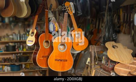 General view of a guitar workshop with hanging wooden guitars and many unassembled parts on the carpentry table with the back wall full of tools Stock Photo