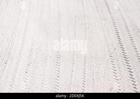 Vehicle tire patterns in white sand. The wheels have made a triangle pattern and multiple lines. There's a slight curve to the pattern. Stock Photo