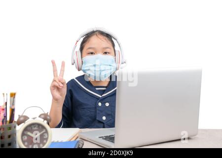 Schoolgirl wears sanitary mask studying online with laptop isolated on white  background,  e-learning  and Covid 19 or coronavirus quarantine. Stock Photo
