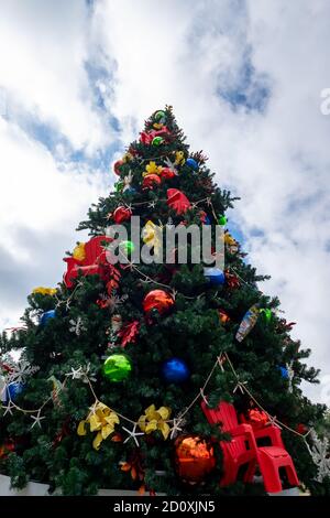 A large artificial Christmas tree decorated with colorful balls, plastic garden chairs, and bows. Stock Photo