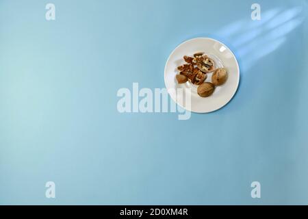 Walnuts, shelled and destroyed, on a white ceramic saucer, on a blue background. Stock Photo