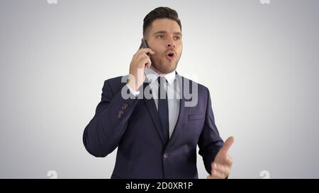 Serious worried businessman talking on cellphone on gradient bac Stock Photo