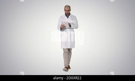 Mature male doctor holding digital tablet using it and walking o Stock Photo