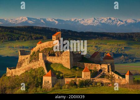 Famous Rupea fortress at sunrise. Stunning castle and high snowy Fagaras mountains in background, Brasov region, Transylvania, Romania, Europe Stock Photo