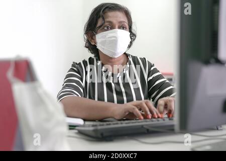Businesswoman wearing face mask typing on computer keyboard Stock Photo