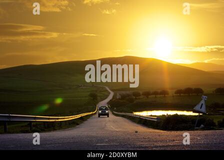 a straight and long rural road travel a scenic landscape of the Sicily in the sunset Stock Photo