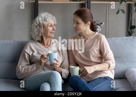Happy mature woman with adult daughter drinking tea at home Stock Photo