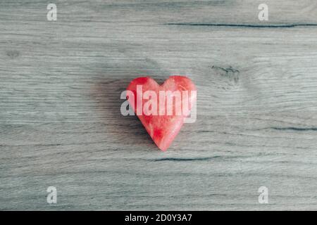 Watermelon slice in the shape of a heart on a wooden background. Minimal art concept. Valentine's day. Flat lay, top view. Stock Photo