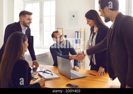 Smiling business partners shaking hands after successful negotiations with colleagues in office Stock Photo