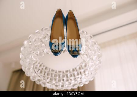 Blue shoes of the bride with a buckle on a glass chandelier. Stock Photo