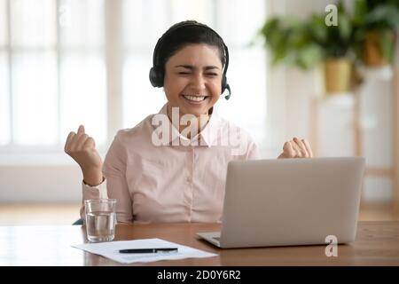 Excited indian female in headphone excited with good news online Stock Photo