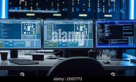 Shot of Multiple Personal Computer Monitors Showing Coding Language Program with System Monitoring Interface. In the Background Data Center with Stock Photo