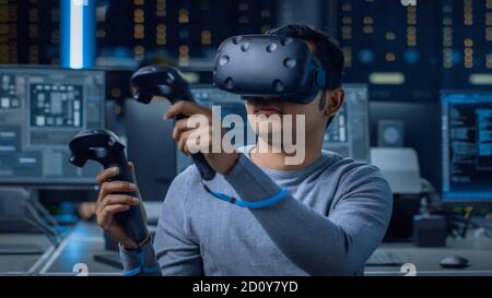 Software Delevoper Wearing Virtual Reality Headset Using Controllers to Develop and Program VR Gaming and Applications. In the Background Technology Stock Photo