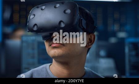 Close-up Portrait of Software Delevoper Wearing Virtual Reality Headset to Develop and Program VR Gaming and Applications. In the Background Stock Photo