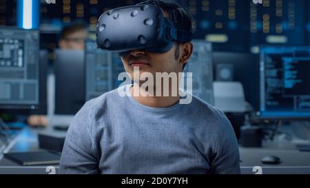 Software Delevoper Wearing Virtual Reality Headset Using Controllers to Develop and Program VR Gaming and Applications. In the Background Technology Stock Photo
