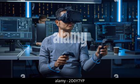 Portrait of Software Delevoper Wearing Virtual Reality Headset Using Controllers to Develop and Program VR Gaming Applications. In Background Stock Photo