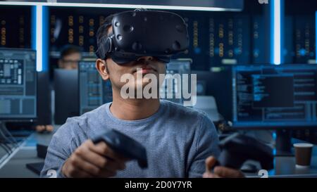 Portrait of Software Delevoper Wearing Virtual Reality Headset Using Controllers to Develop and Program VR Gaming Applications. In Background Stock Photo