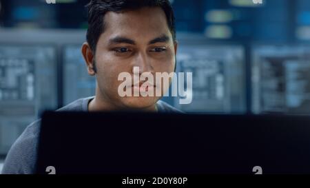 Portrait of a Smart and Handsome IT Specialist Working on a Personal Computer. In the Background Unfocused Personal Computers with Screens in Stock Photo