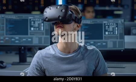 Software Delevoper Wearing Virtual Reality Headset Gesturing with His Head, Developing and Programming VR Game or Application. In Background Stock Photo