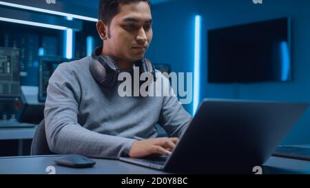 Portrait of Software Developer Hacker Programmer Sitting at His Desk and Working on Laptop Computer In the Background Dark Neon High Tech Environment Stock Photo