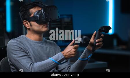 Portrait of Software Delevoper Wearing Virtual Reality Headset Using Controllers to Develop and Program VR Gaming and Applications. In Background Stock Photo