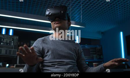 Software Delevoper Wearing Virtual Reality Headset Gesturing with His Head, Developing and Programming VR Game or Application. In Background Stock Photo