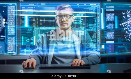 Portrait of Software Developer Hacker Wearing Glasses Sitting at His Desk and Working on Futuristic Transparent Computer in Digital Identity Cyber Stock Photo