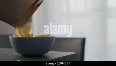 pour potato chips from paper bag into blue bowl on concrete countertop, wide photo Stock Photo