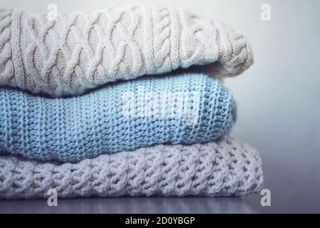 On the gray table, three warm wool sweaters with different patterns are stacked in a pile, ready for the cold. Winter time. Stock Photo