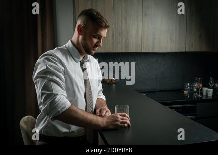 Handsome man wearing suit, drinking whiskey on the kitchen at home