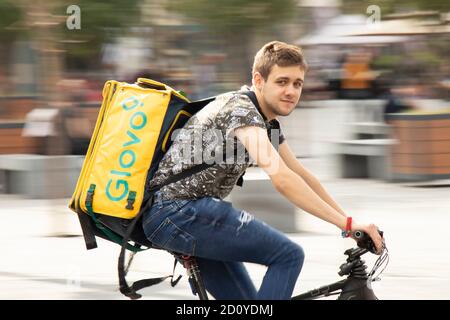 Belgrade, Serbia - October 02, 2020: Young courier working for Glovo city food delivery service riding a bicycle on city street Stock Photo