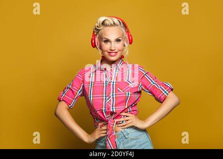 Happy blonde pin-up model woman listening music with headphones on yellow background Stock Photo