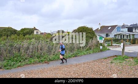 Worthing UK 4th October 2020 -  Runners in the Virtual London Marathon battle against the elements on a wet and windy day along Ferring seafront near Worthing  : Credit Simon Dack / Alamy Live News . Stock Photo