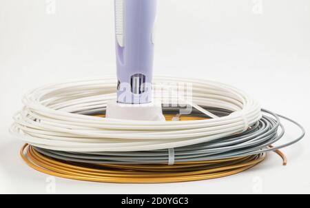 Closeup view of multicolored rolled cables around childrens 3D printing pen isolated on white. Bright filament plastic lying indoors. Concept children Stock Photo