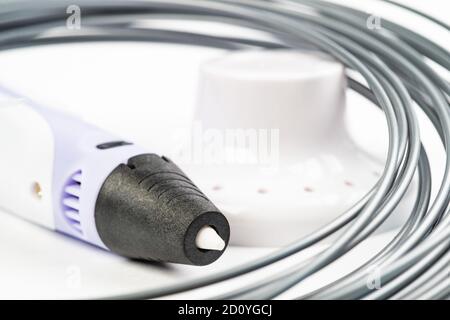 Closeup view of colorful rolled cables and childrens 3D printing pen isolated on white. Three bright filament plastic lying indoors, studio background Stock Photo