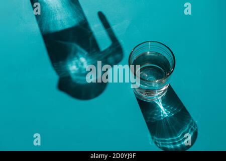 A glass with water next to a jug on a light blue background where its shadows are cast Stock Photo