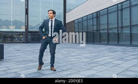 Cheerful and Happy Businessman in a Suit is Actively Dancing on a Street Square. Scene Shot in an Urban Concrete Park Next to Business Center. Sunny Stock Photo