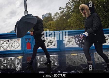 Tourists battle through the wind and rain on Tower Bridge in central London as the UK's wet weekend continues and a weather warning for rain across parts of Wales and England has been extended. Stock Photo