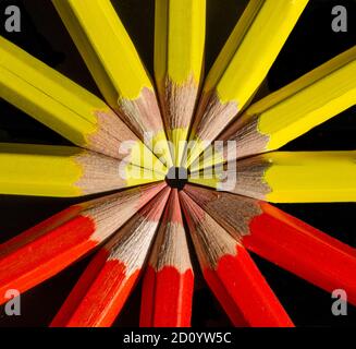Yellow and red colored pencils in the round formation on the black background close up .Macro photography. Stock Photo