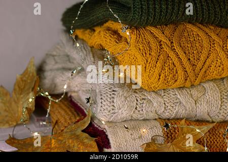 Warm colorful sweaters, yellow leafs and decorative lighting. Autumn concept composition. Stock Photo