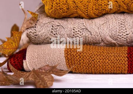 Stack of warm woolen colorful knitted winter and autumn sweaters with dray leaves autumn background close up image. Stock Photo
