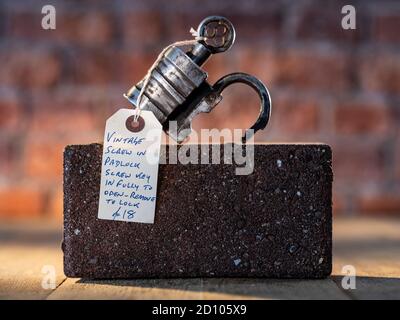 Vintage Barrel Padlock with screw key resting on brick with brick background on timber floorboards Stock Photo